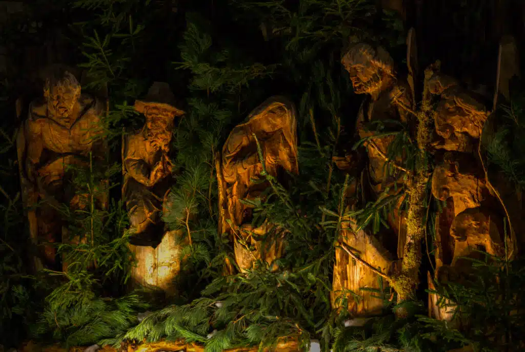 Large hand-carved wooden nativity figures lit among fir branches at the Bruneck Christmas Market at night