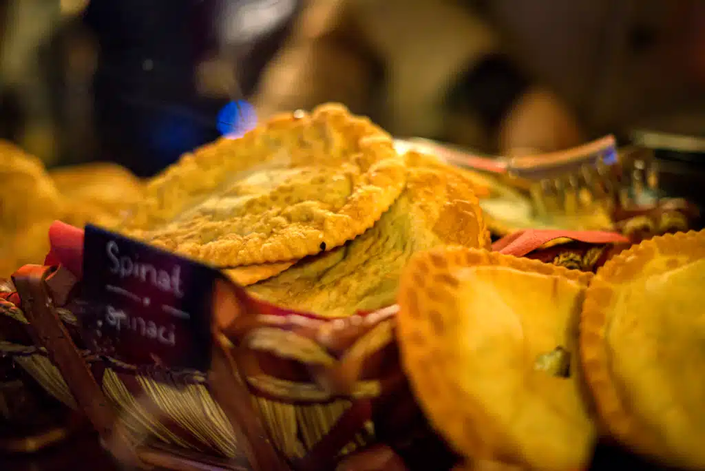 Spinach Tirtlan (fried South Tyrolean pastries) in a basket at the Bruneck Christmas Market, with a Spinat / Spinaci sign
