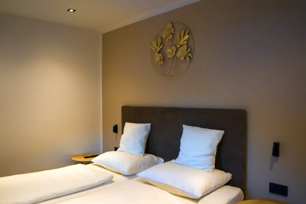 Bedroom at Appartements Hofer with twin beds made up in white linens, a dark upholstered headboard, and gold floral wall art.