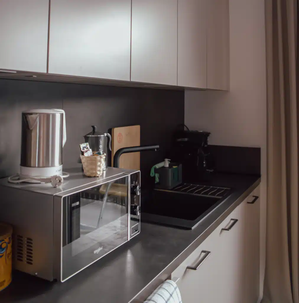 ompact kitchenette at Appartements Hofer with electric kettle, microwave, coffee maker, and black sink, set up for self-catering during a Val Pusteria winter stay.