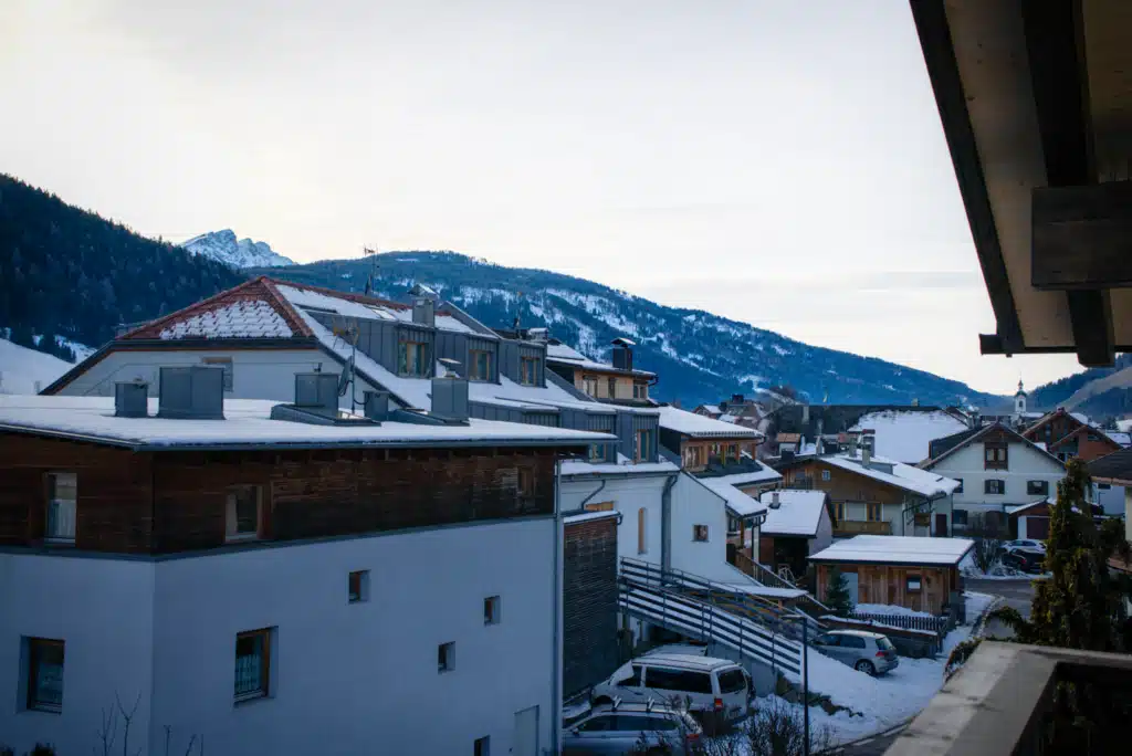 Snow-covered rooftops and surrounding Dolomite peaks seen from the balcony of Appartements Hofer in Dobbiaco, Val Pusteria, on a winter afternoon.
