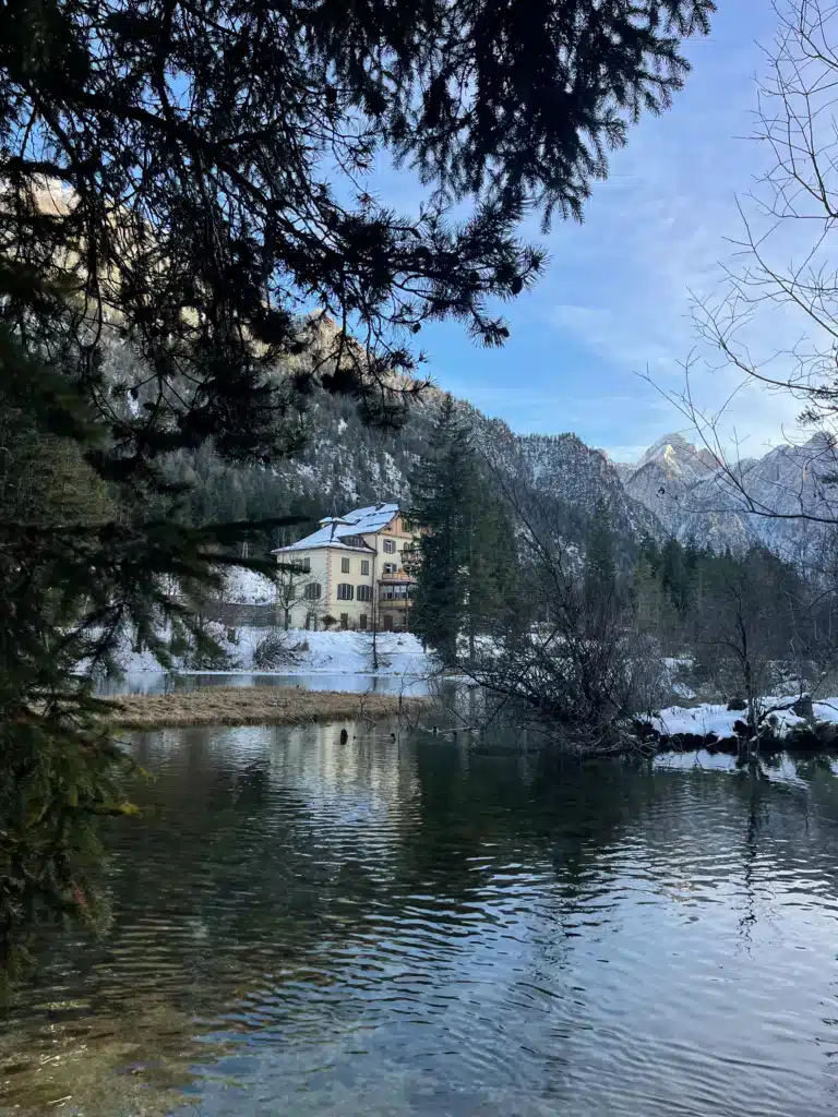 Historic cream-coloured lakeside hotel framed by pines across the water at Lago di Dobbiaco in winter, South Tyrol.