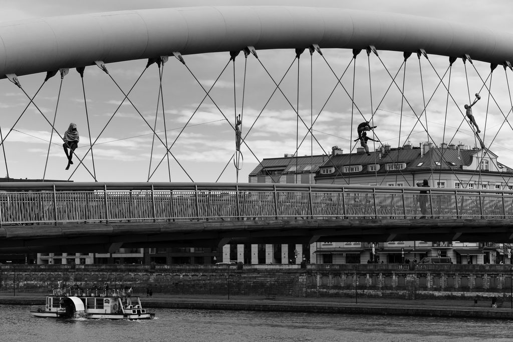 Artistic black and white photo of Bernatka Footbridge, Kraków with acrobat sculptures.