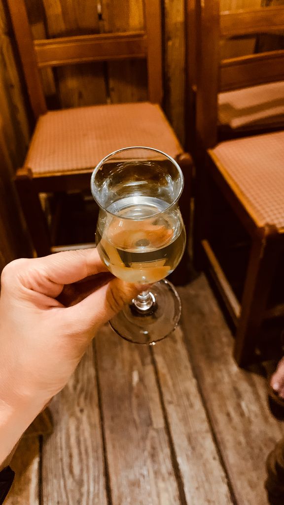 Close-up of a hand holding a wine glass indoors with rustic wooden chairs.