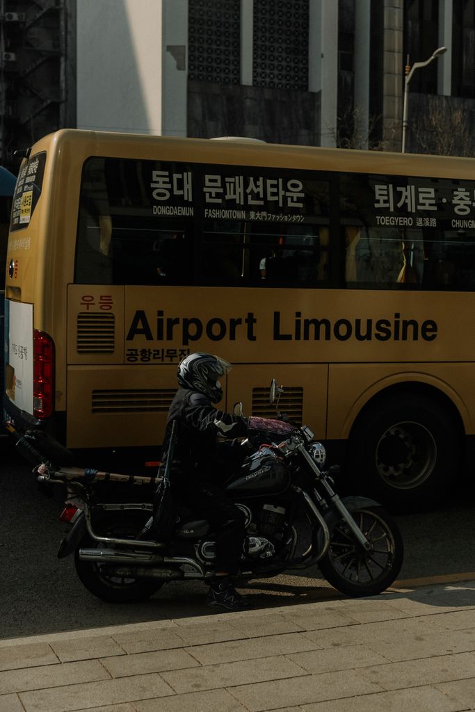 Motorcyclist passes airport bus on bustling South Korean city street during the day.