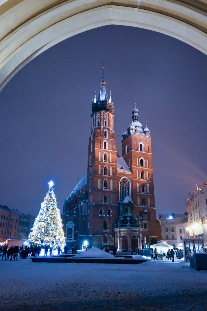 Stunning winter scene of St. Mary's Basilica in Krakow at night, adorned with festive lights.