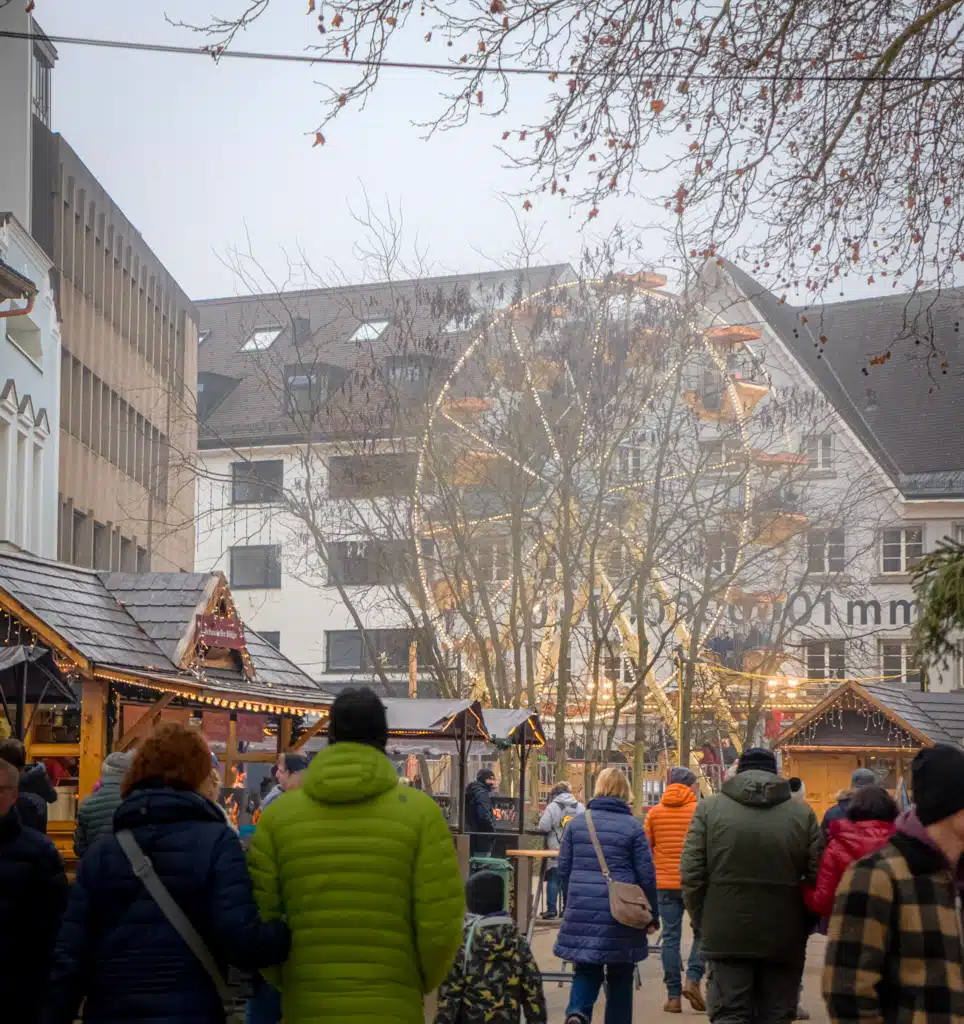 Foggy view of Bregenz Christmas market stalls with Ferris wheel behind bare trees
