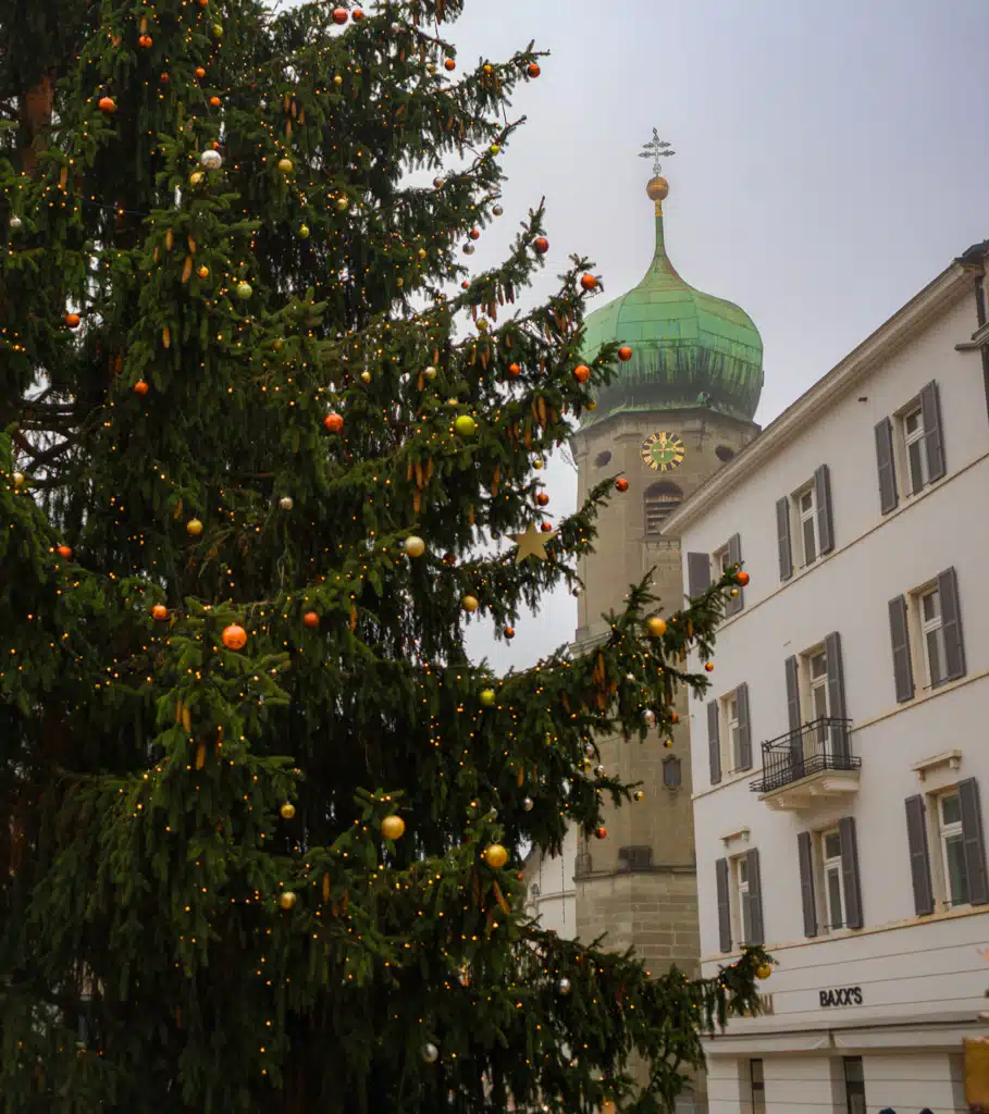 Decorated Christmas tree with green-domed church tower in Bregenz old town