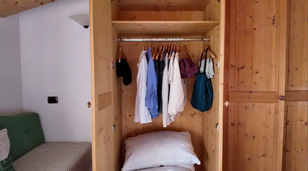 Open wardrobe closet at Ütia de Börz with hanging clothes, coat hooks, and stored pillows