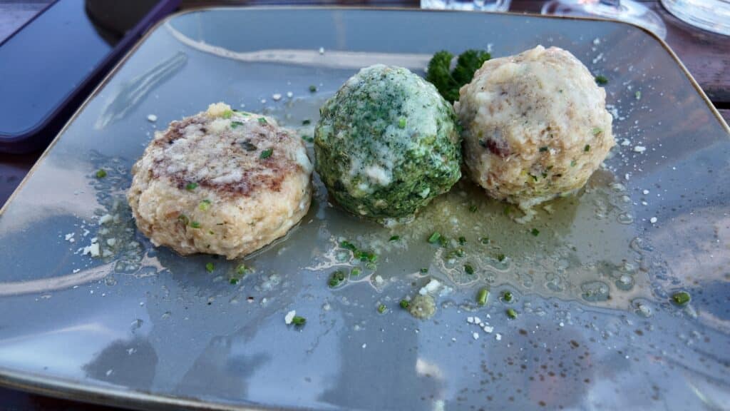 Three South Tyrolean canederli dumplings, plain, spinach, and speck, served at a mountain rifugio