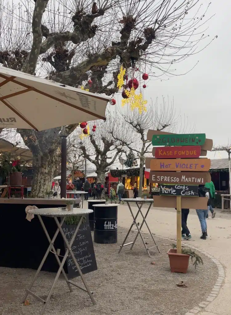 Wooden signpost listing Glühwein, Käsefondue, and cocktail options at Konstanz Christmas Market