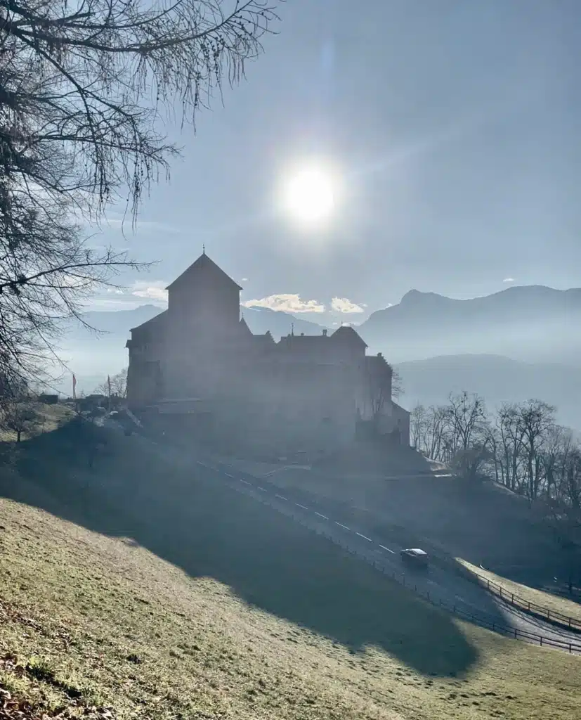 Vaduz Castle silhouetted against the sun with Alpine mountains in the background