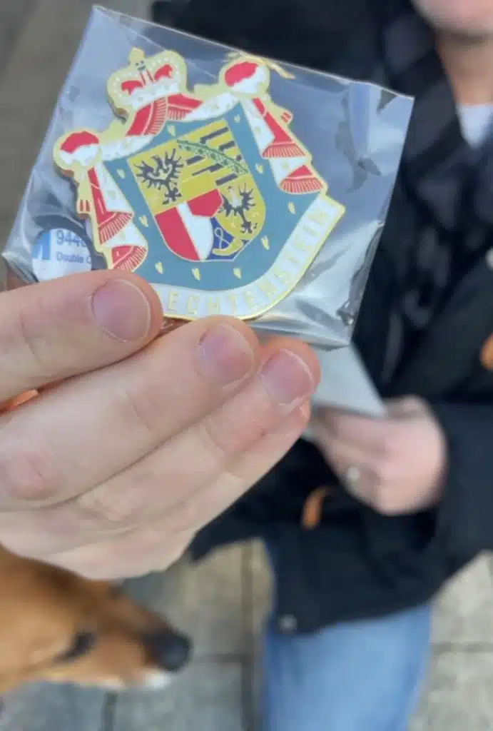 Hand holding enamel pin with Liechtenstein coat of arms souvenir