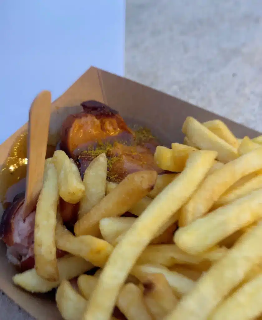 A cardboard tray of currywurst and fries with curry powder and sauce at the Lindau Christmas market