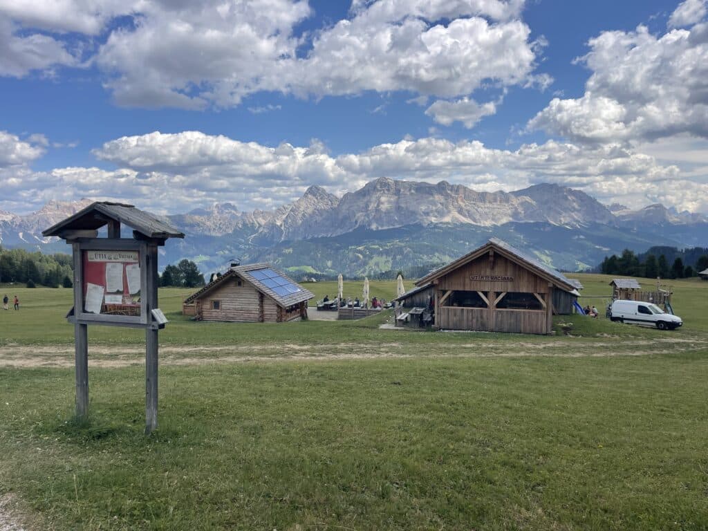 Ütia Vaciara wooden mountain huts with outdoor seating and a Dolomites mountain range in the background