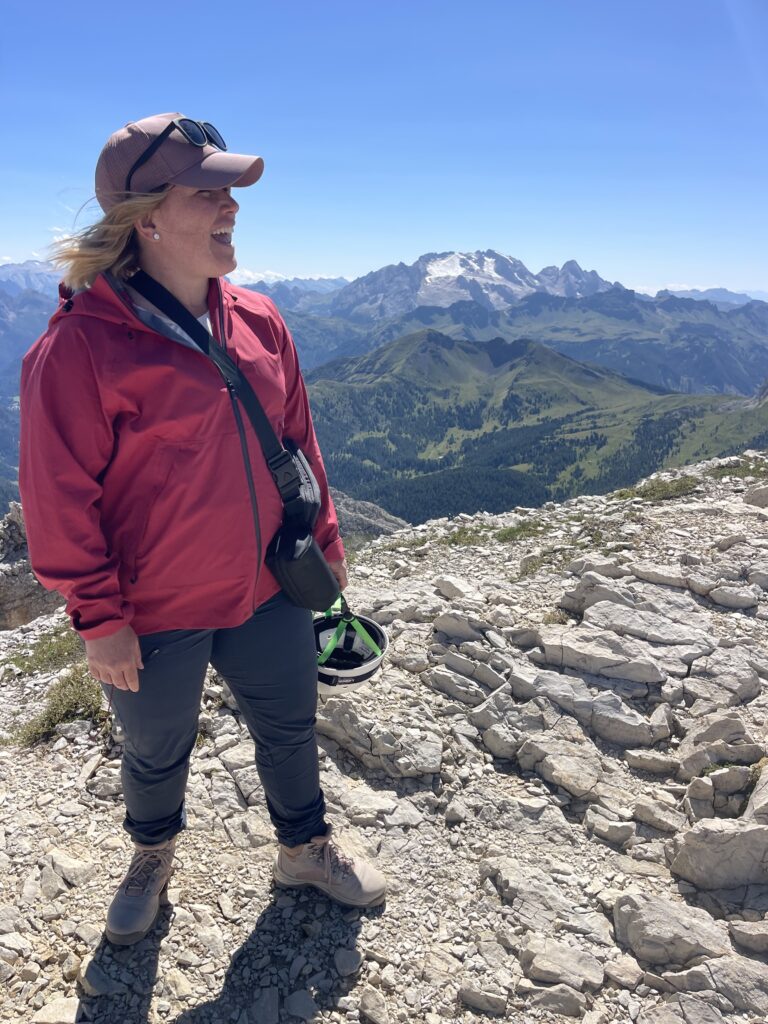 Woman in a red rain jacket and pink cap holding a helmet with headlamp at Rifugio Lagazuoi