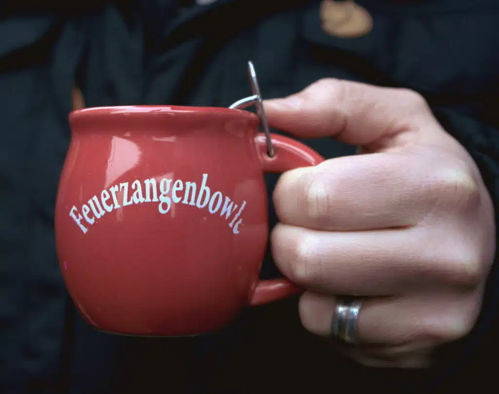 A hand holding a red Feuerzangenbowle mug with its sugar tongs at the Lindau Christmas market