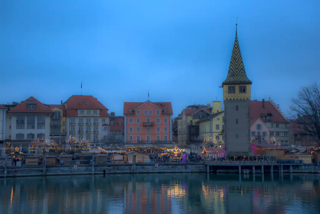 The Lindau Christmas market lights reflected in the harbour at blue hour, with the Mangturm tower above