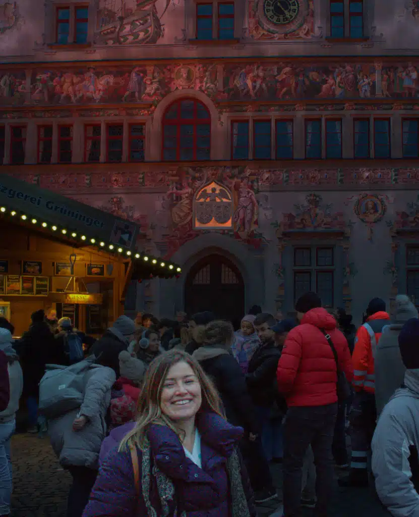 Woman in navy Uniqlo puffer jacket smiling in front of the painted Lindau Rathaus facade at Christmas market