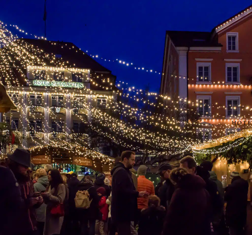 Thousands of fairy lights strung above the crowd at the Lindau Christmas market at blue hour