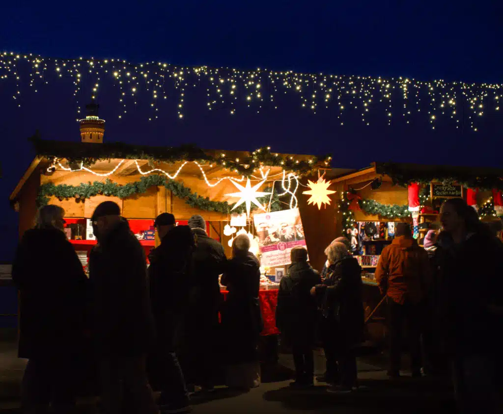 Shoppers silhouetted against glowing wooden stalls and paper stars at the Lindau Christmas market at dusk