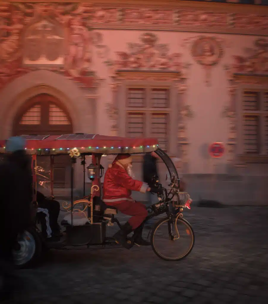 A person dressed as Santa pedals a decorated rickshaw past the frescoed Altes Rathaus at the Lindau Christmas market