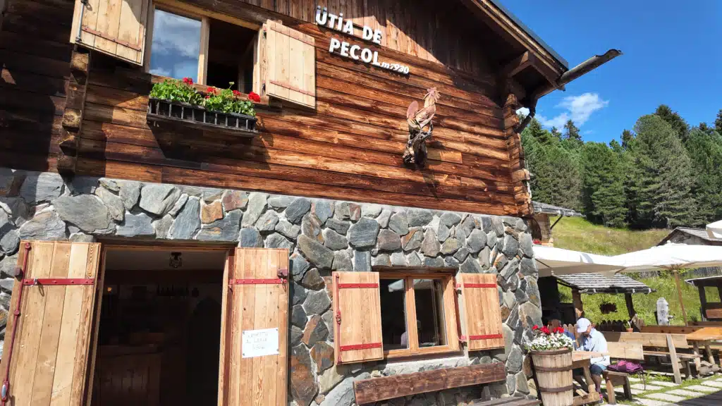 Front exterior of Ütia de Pecol mountain hut at 1,930m with wooden rooster decoration and stone facade