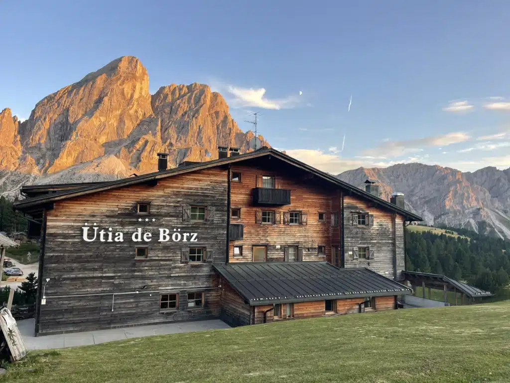 Ütia de Börz hotel exterior at golden hour with Sass de Putia peak glowing behind it in the Dolomites