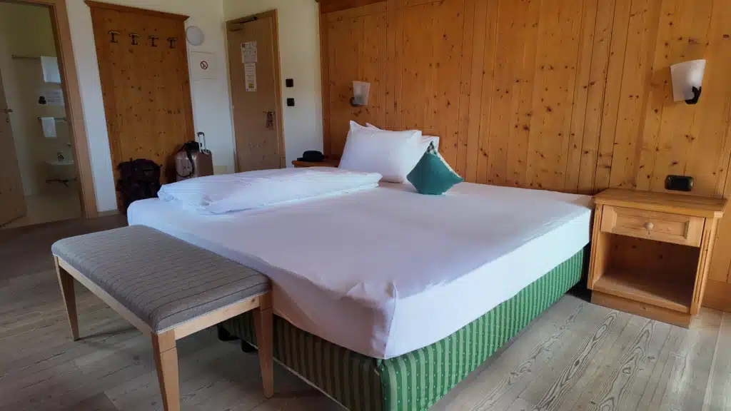 Double Room with Balcony at Ütia de Börz, pine-paneled walls and green-striped bed frame