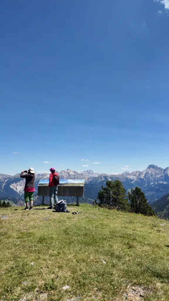 Hikers reading a panoramic viewpoint board overlooking the Dolomites near Ütia de Pecol