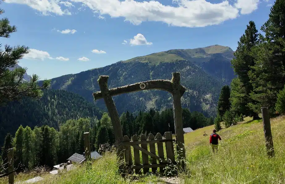 Wooden trail gate with mountain views on the path to Ütia de Pecol, hiker approaching