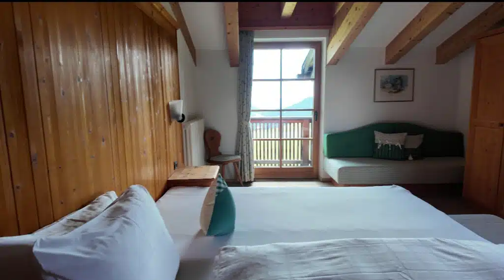 Wide view of a Double Room with Balcony at Ütia de Börz, the bed, wood beams, and a green daybed