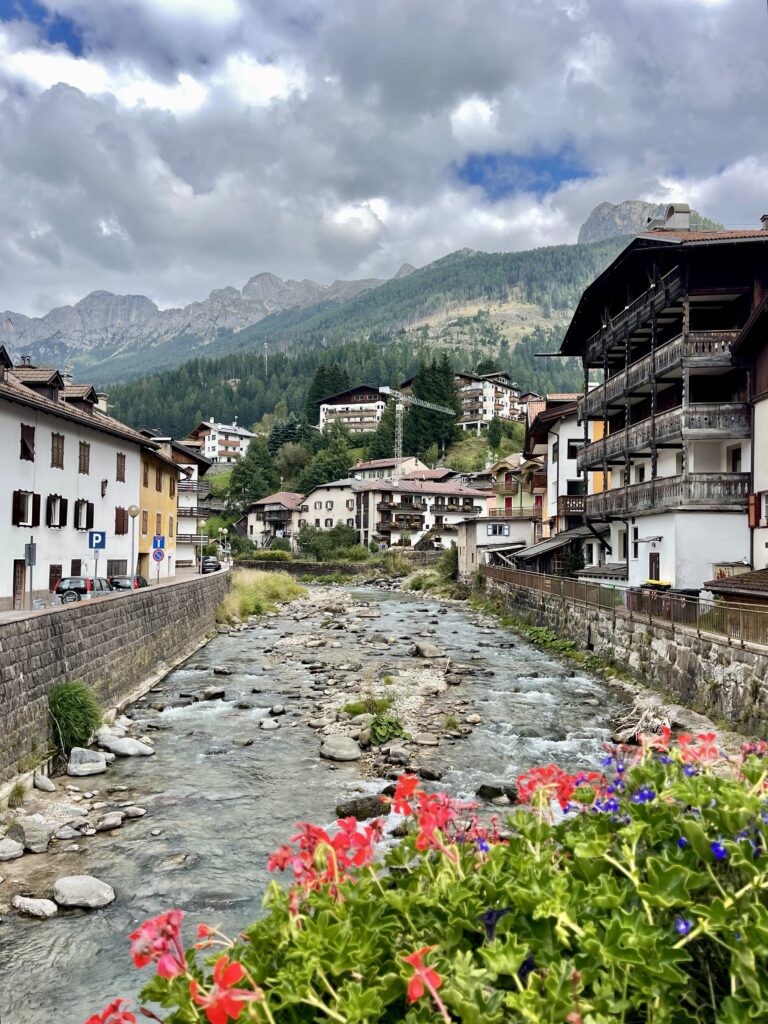 The river running through Moena, with geraniums, wooden balconies and Dolomite peaks behind