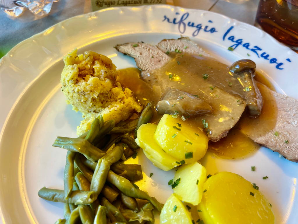 Dinner plate at Rifugio Lagazuoi with pork loin, mushroom gravy, boiled potatoes, green beans, and polenta