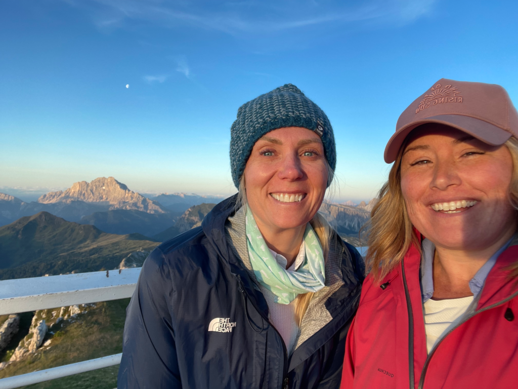Two women smiling together with the Dolomites lit by Evening lite behind them