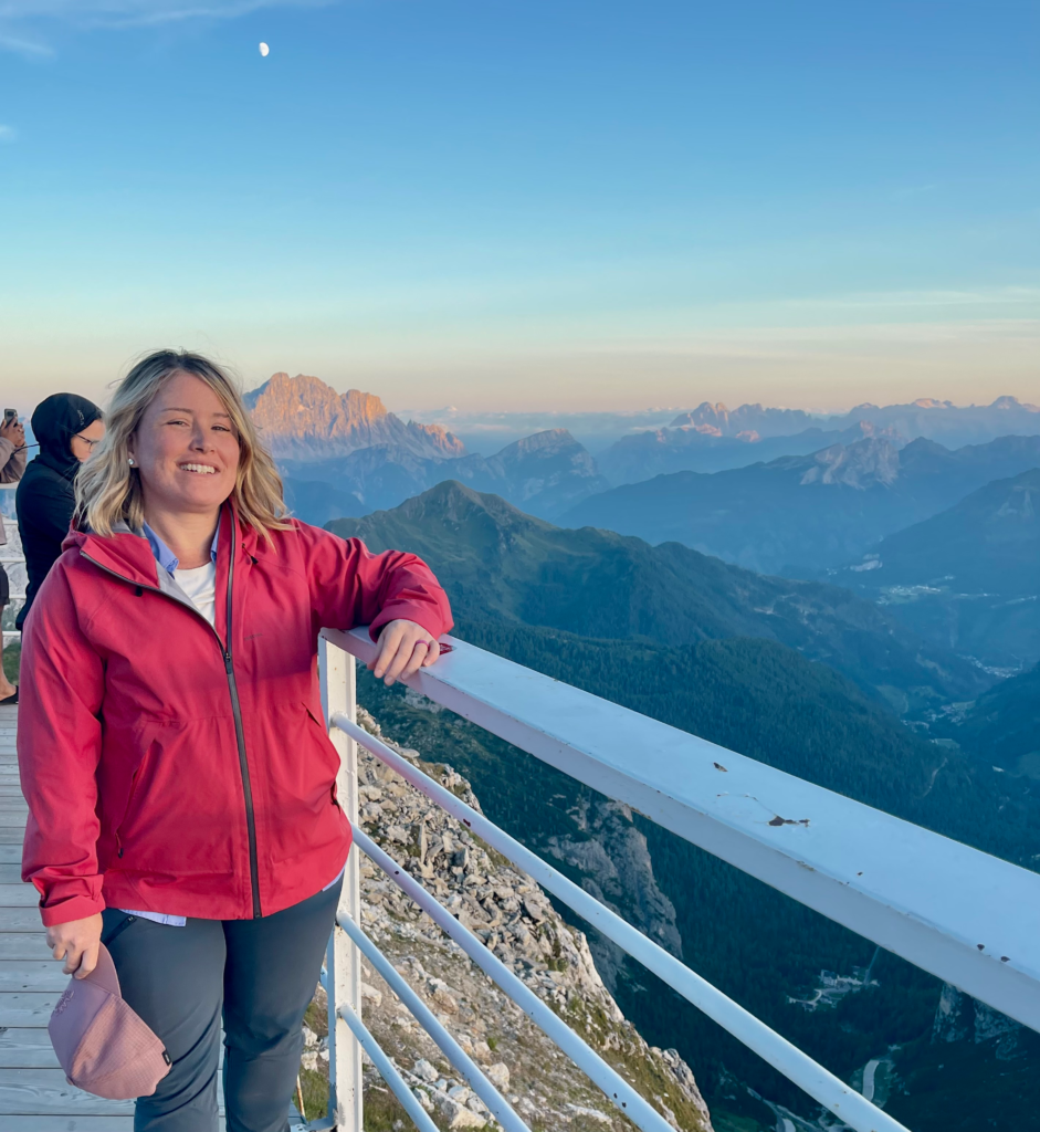Woman leaning on a railing overlooking the Dolomites during sunset at Rifugio Lagazuoi