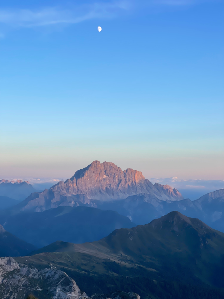 A Dolomites peak lit by alpenglow with the moon above at dusk