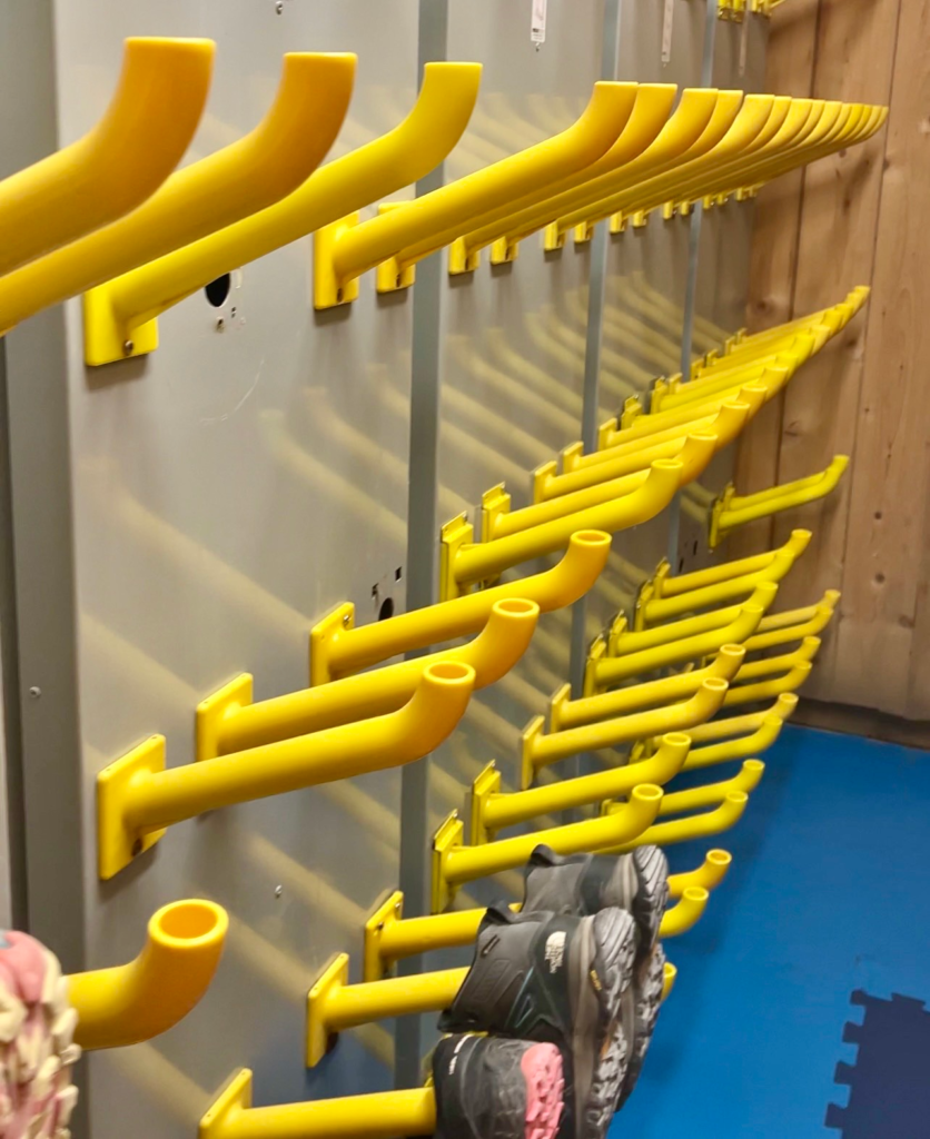 Rows of yellow wall hooks for boots and helmets in the Rifugio Lagazuoi shoe room