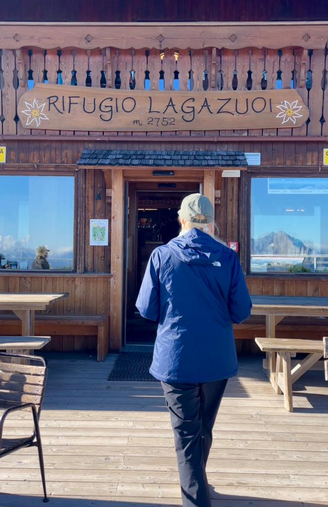 Woman walking toward the wooden Rifugio Lagazuoi entrance sign reading "m. 2752
