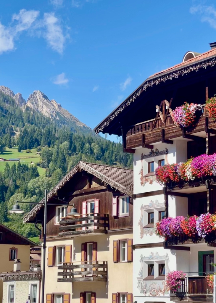Frescoed and wooden-balconied buildings in Moena with Dolomite peaks behind