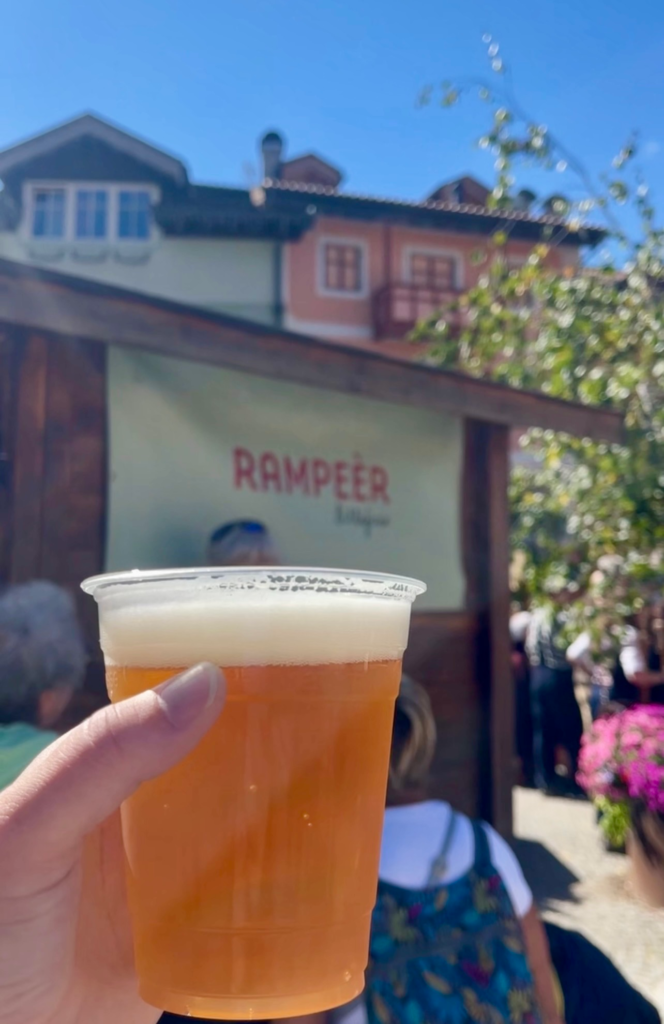 A cup of local beer held up in front of a festival stall in Moena