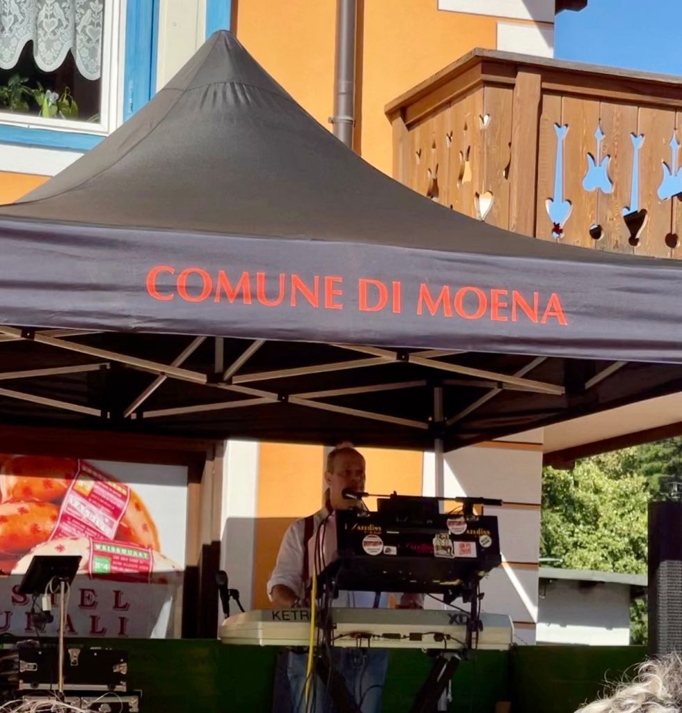A musician performing under a Comune di Moena gazebo at the Puzzone festival