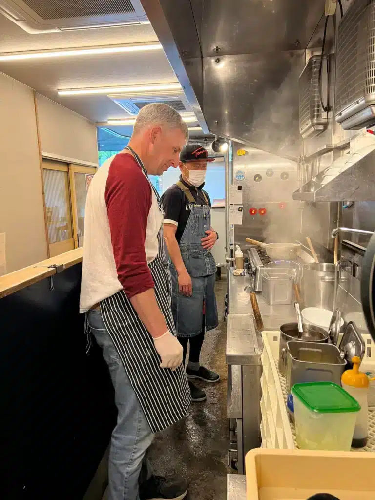 Man in an apron cooking at the stove with the chef supervising during an Osaka ramen class