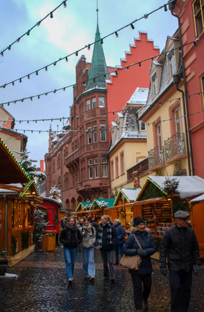 Wooden stalls and string lights along a snowy cobblestone lane at the Freiburg Christmas market in Germany's Black Forest