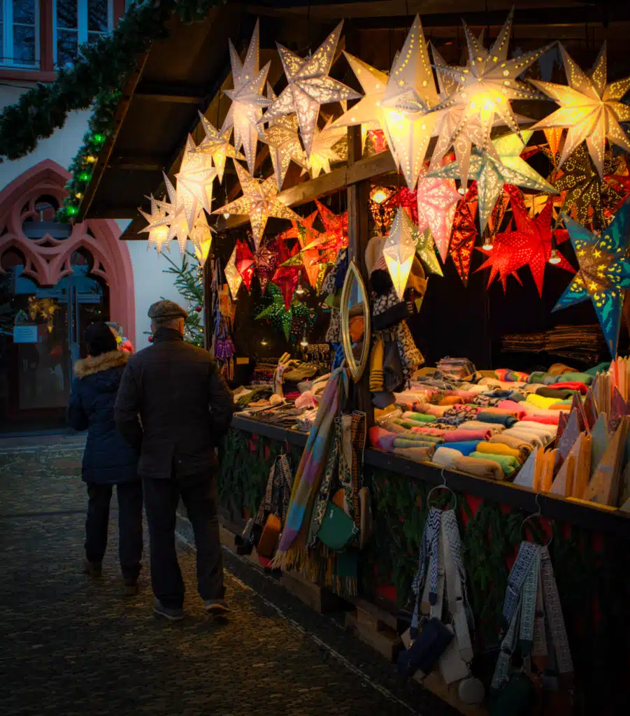 Lit paper star lanterns and wool scarves for sale at a stall at the Freiburg Christmas market at dusk