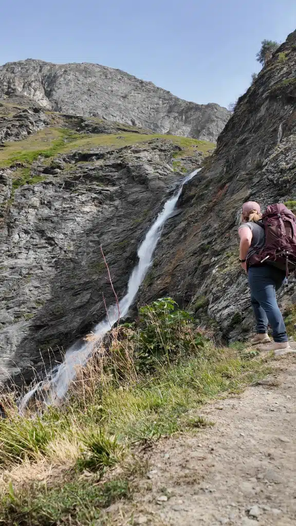 Solo female hiker with an Osprey pack stopping to look at a waterfall on day 3 from Refuge de Plaisance to Refuge de la Glière, Tour du Vallaisonnay