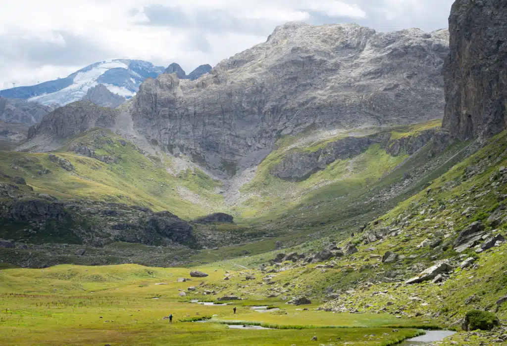 Two fishermen standing in the wide green valley below Lac de la Plagne, with glaciated peaks and grey rock walls rising behind them, on day one of the Tour du Vallaisonnay in Vanoise National Park.